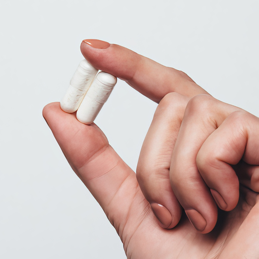 Two supplement capsules held in between the index finger and thumb of a person's hand.